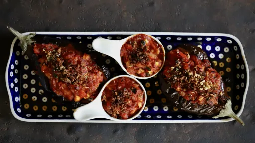 Danie wegańskie vegestyl: pieczone bakłażany z sosem pomidorowym na ozdobnym talerzu.