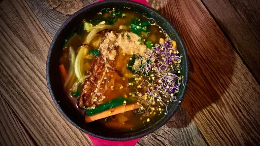 Wegański ramen vegestyl z warzywami i makaronem na drewnianym stole.